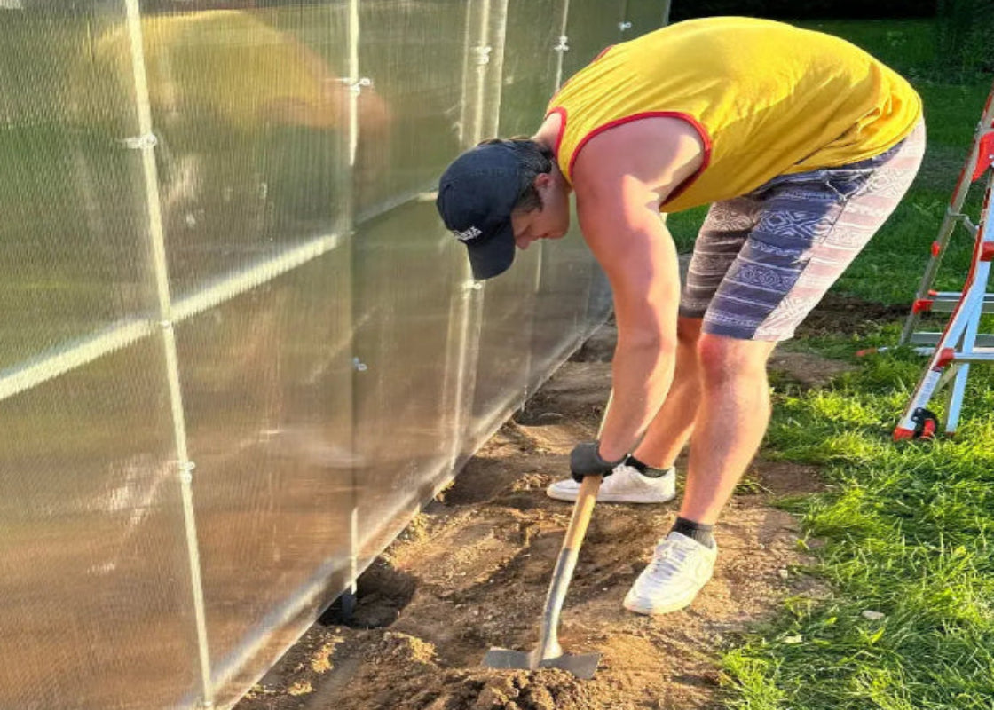 Installing greenhouse ground anchors beside the galvanized steel frame